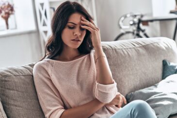 woman sitting on the couch holding her head due to fatigue after quitting alcohol