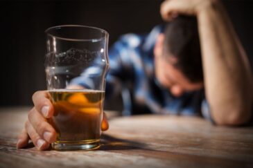 man with alcohol brain fog with head down holding a beer